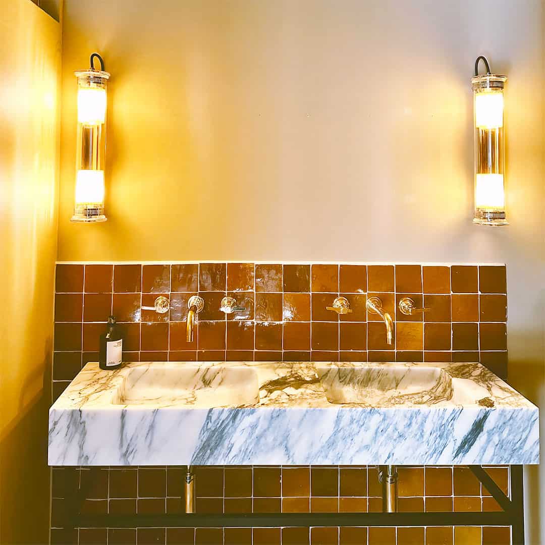 Bathroom sink with marble countertop and tiled wall, illuminated by wall lights.
