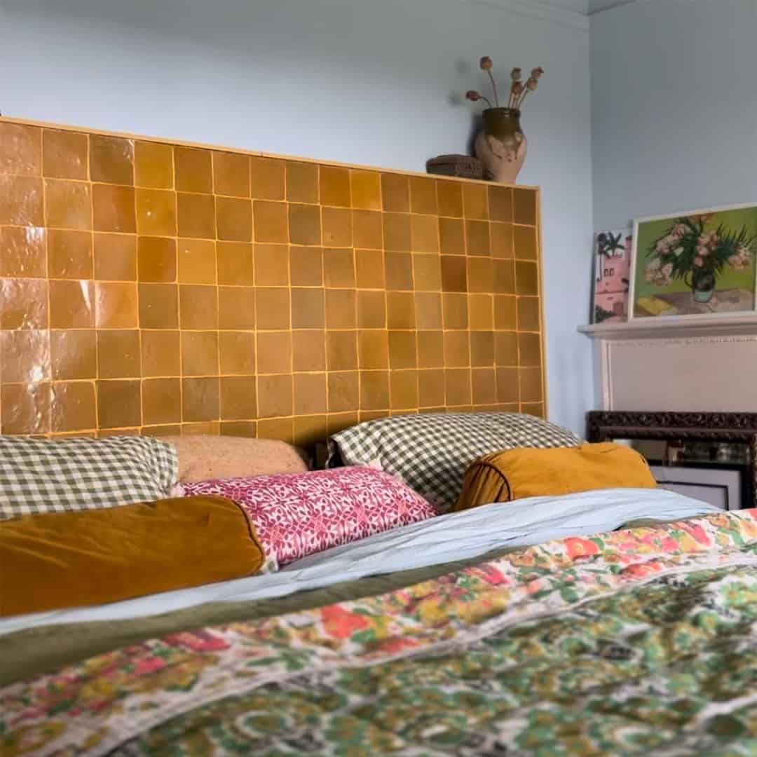 Bed with colorful bedding against a yellow tiled wall in a bedroom setting.