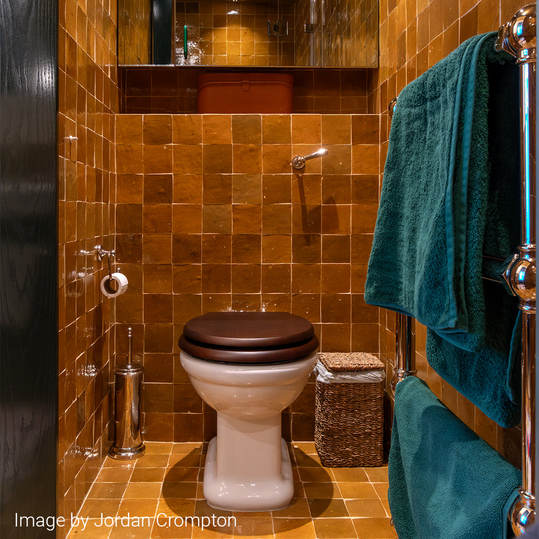 Bathroom with brown tiled walls, toilet, and green towel.