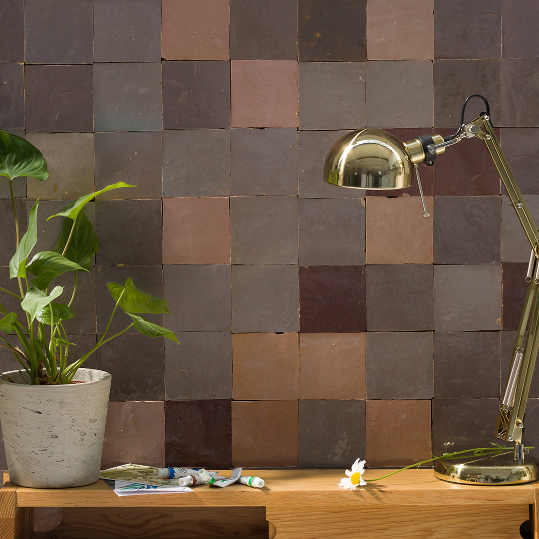 Decorative wall with square tiles in brown and gray, a plant, and a lamp on a wooden surface.