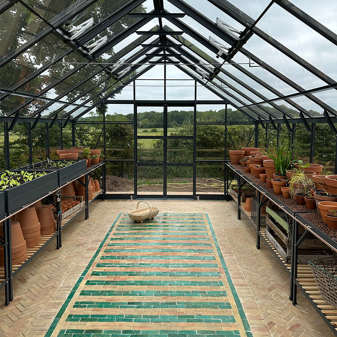 Striped green and beige bathroom mosaic tile flooring inside greenhouse, bordered with green tiles, blending decor and functionality.