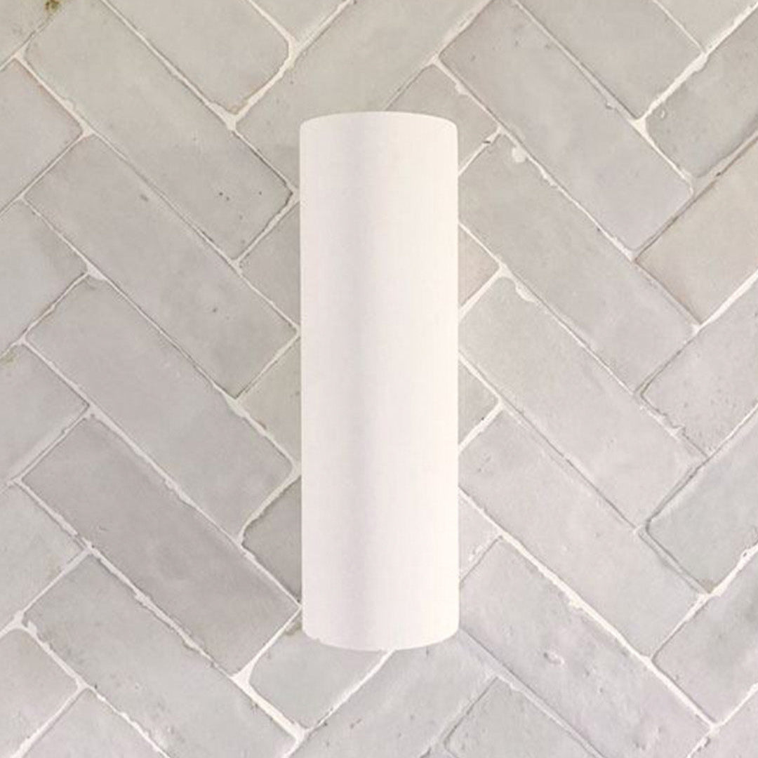White cylindrical light fixture on a tiled wall with a herringbone pattern