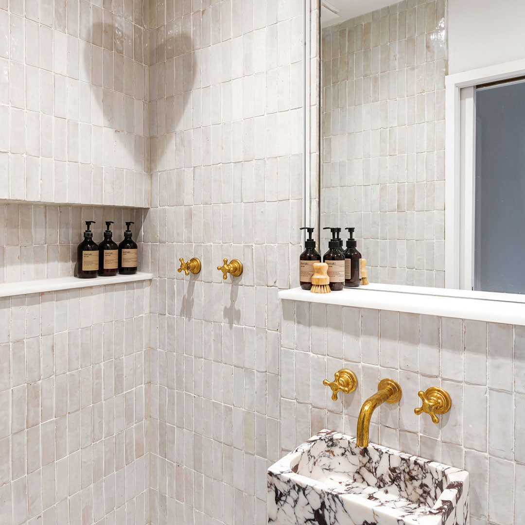 Bathroom with white tiled walls, gold fixtures, and a marble sink.