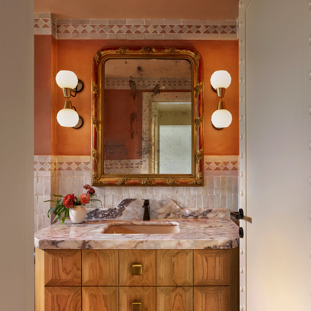 Bathroom vanity with marble countertop, wooden cabinets, and decorative mirror.