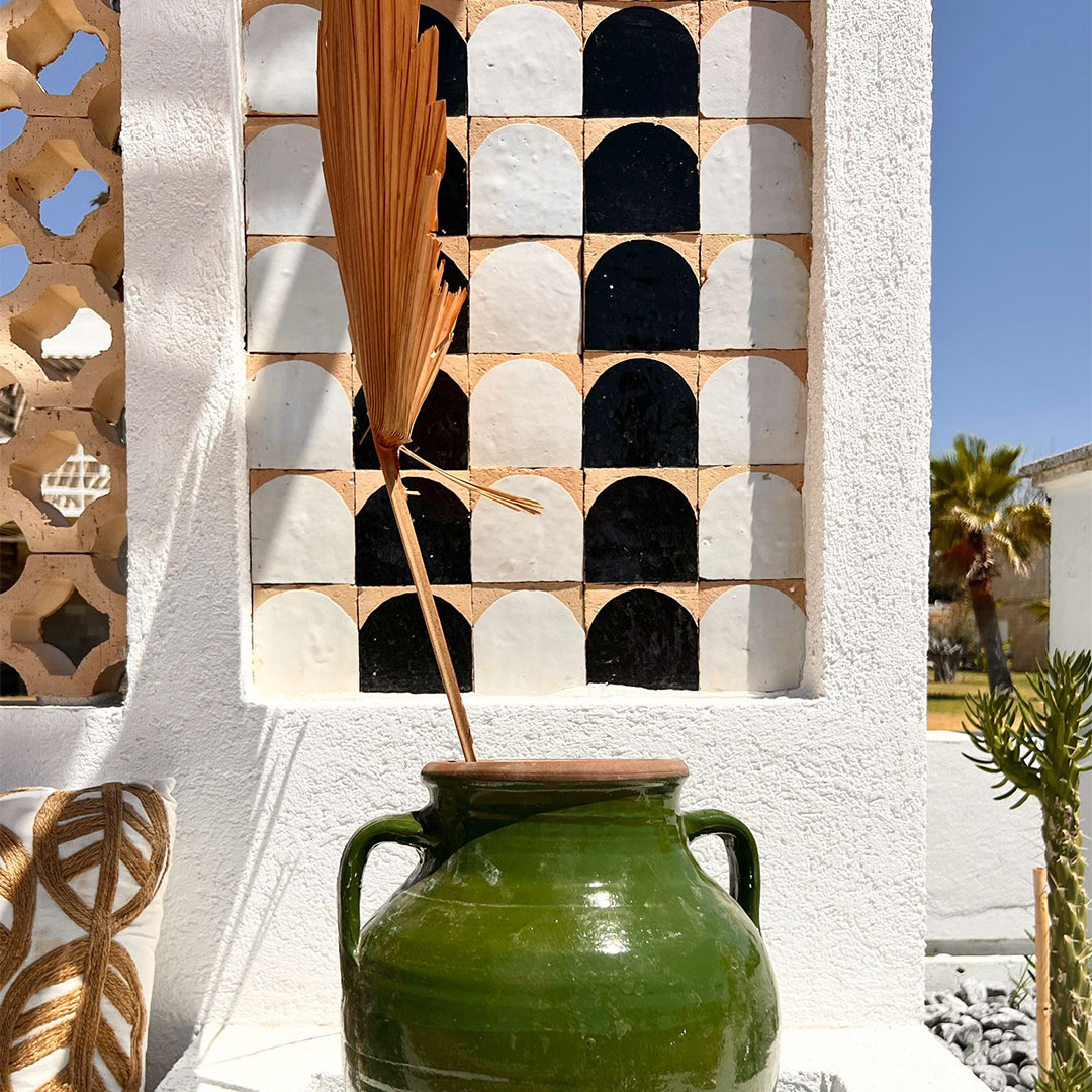 Green ceramic jar with a wooden lid against a decorative wall with geometric patterns.