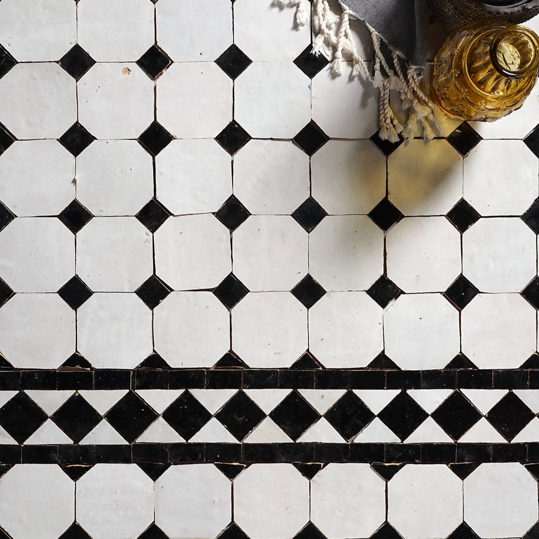 Black and white geometric tile pattern on a floor with a bottle and towel in the corner.