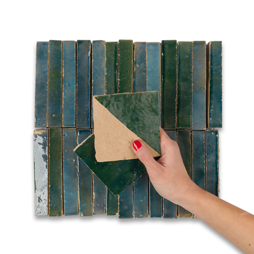 Hand holding a green ceramic tile against a patterned tile background