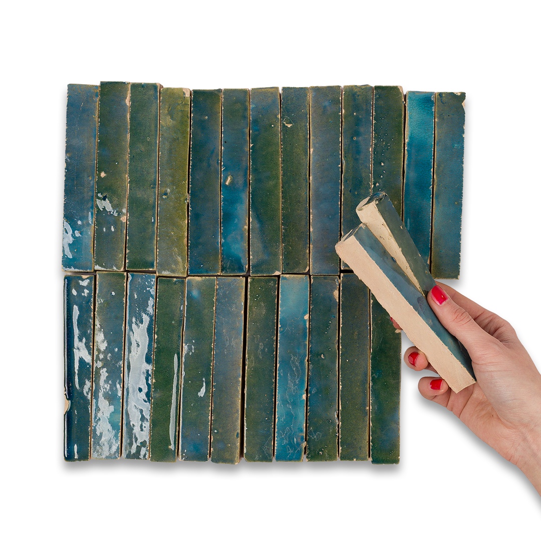 Hand holding a wooden tool over a grid of blue and green ceramic tiles on a white background