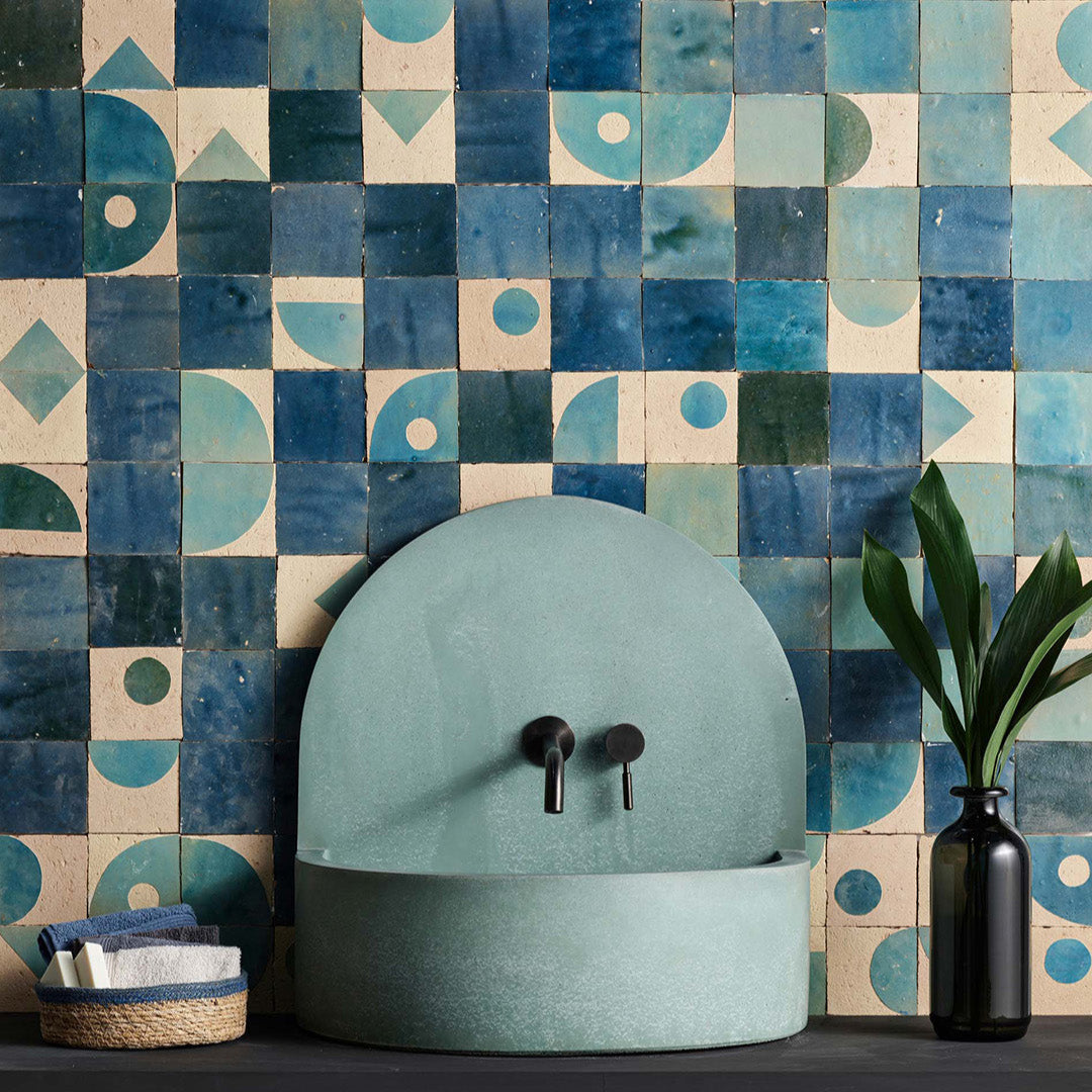 Teal ceramic sink against a geometric blue and beige tiled wall.