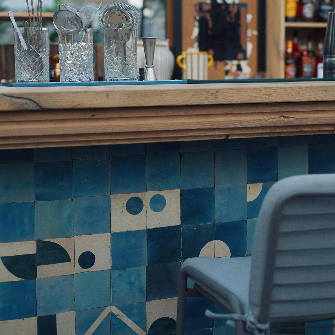 Bar area with geometric blue tile pattern on the wall, bar tools, and a chair.