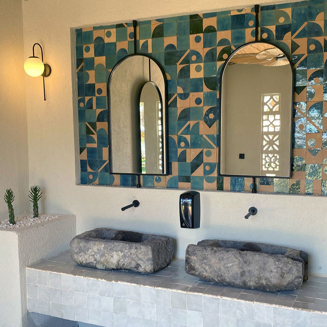 Bathroom with geometric tile pattern, stone sinks, and wall-mounted mirrors.