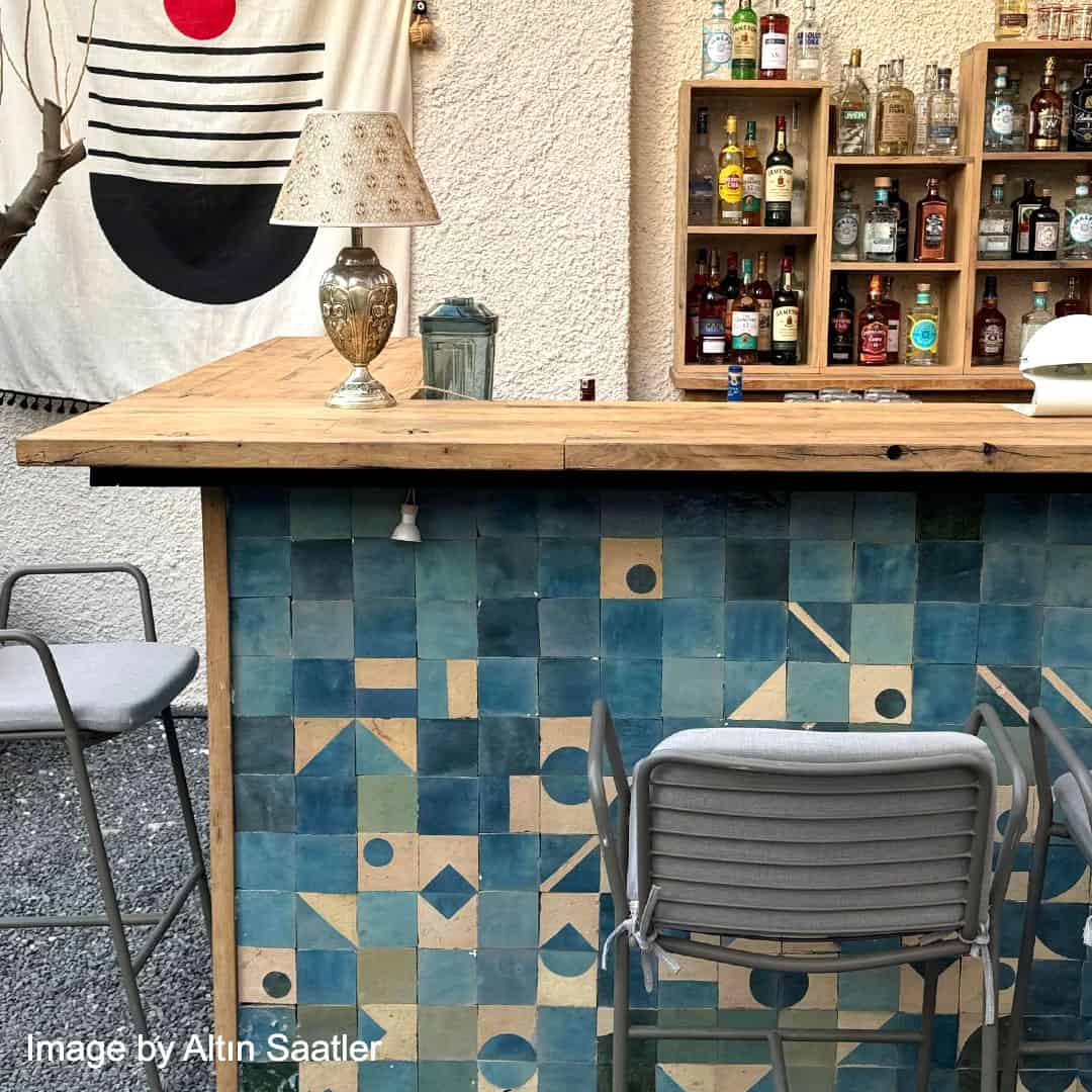 Bar area with wooden counter, geometric blue tile pattern, and shelves with bottles.