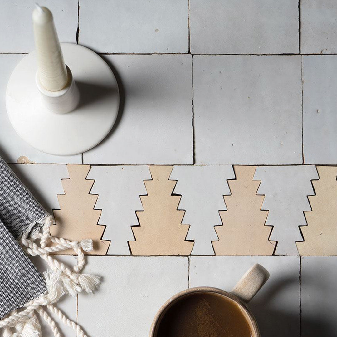 Wooden Christmas tree coasters on a tiled surface with a cup and decorative item.