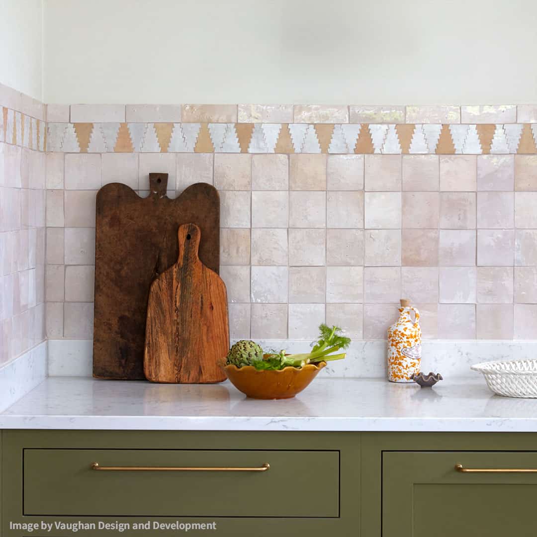 Kitchen counter with wooden cutting boards, a bowl of vegetables, and decorative items against a tiled backsplash.