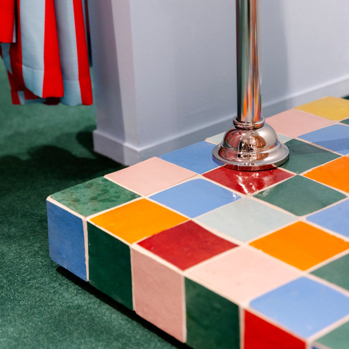 Colorful tiled step with a metallic pole on a green carpeted floor.