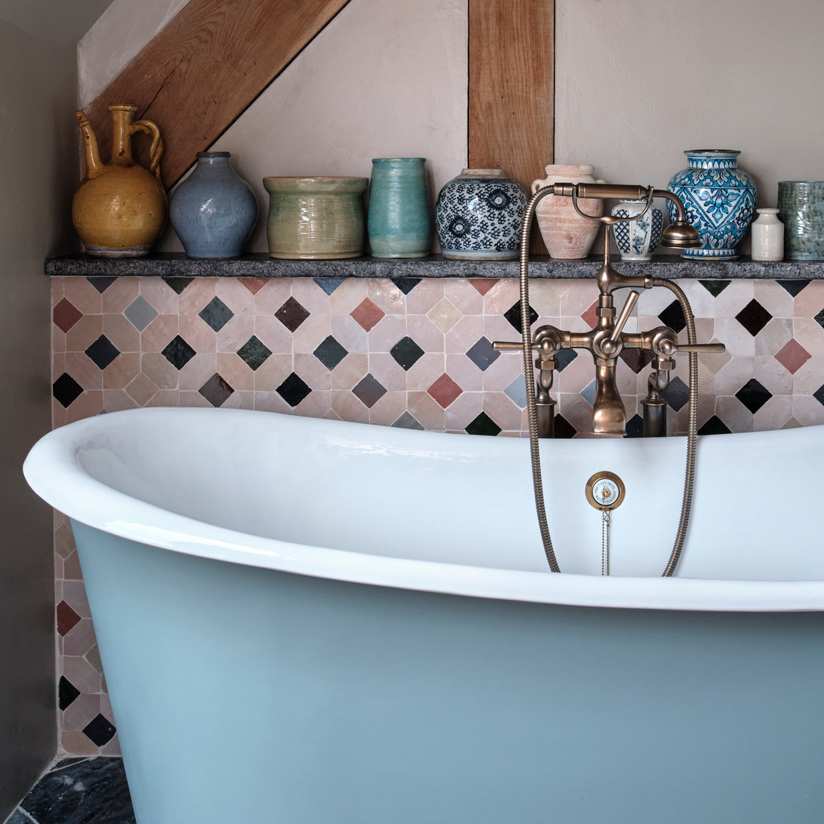 Bathroom with a freestanding bathtub, decorative tiles, and various vases on a shelf.