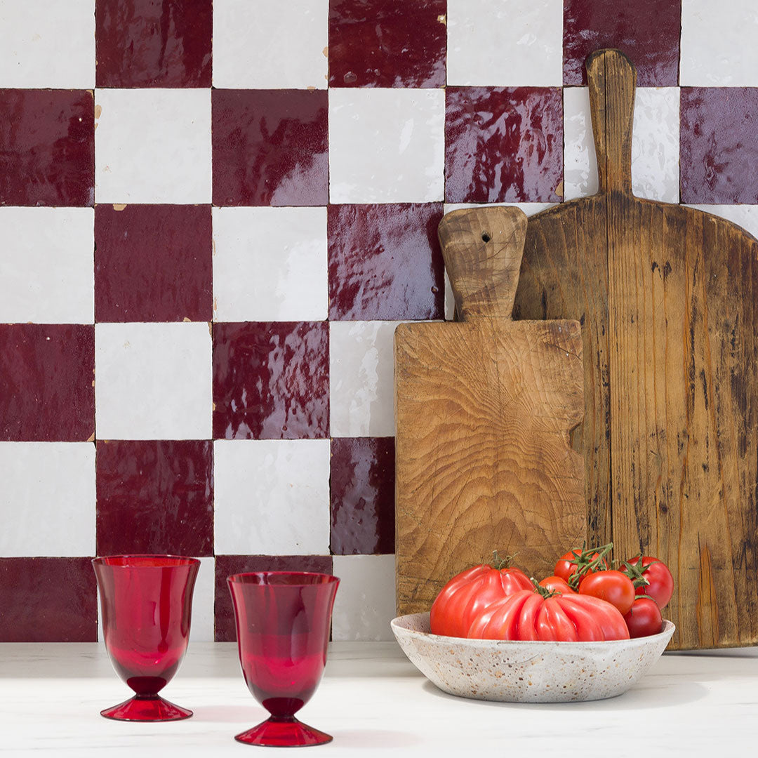 Wooden cutting boards and red tomatoes on a white surface with a checkered red and white wall.