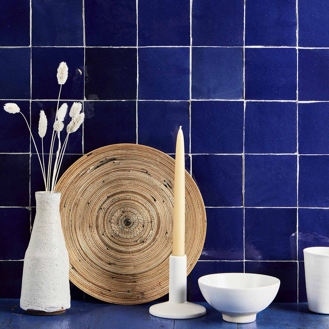 Deep blue bathroom wall tiles with white grout, styled with ceramic vase, dried flowers, candle, and minimalist accessories.