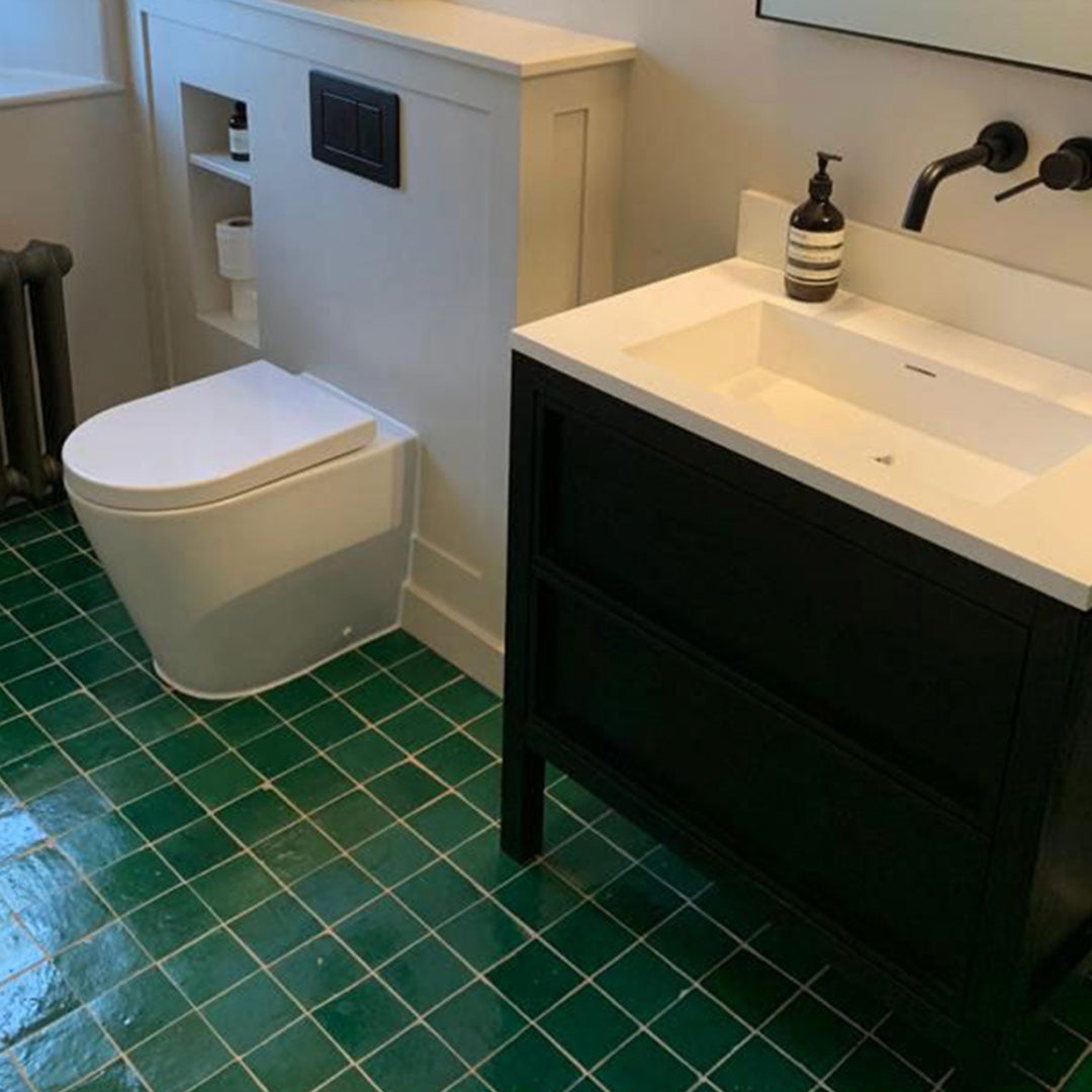 Bathroom with green tiled floor, white toilet, and black vanity with sink.