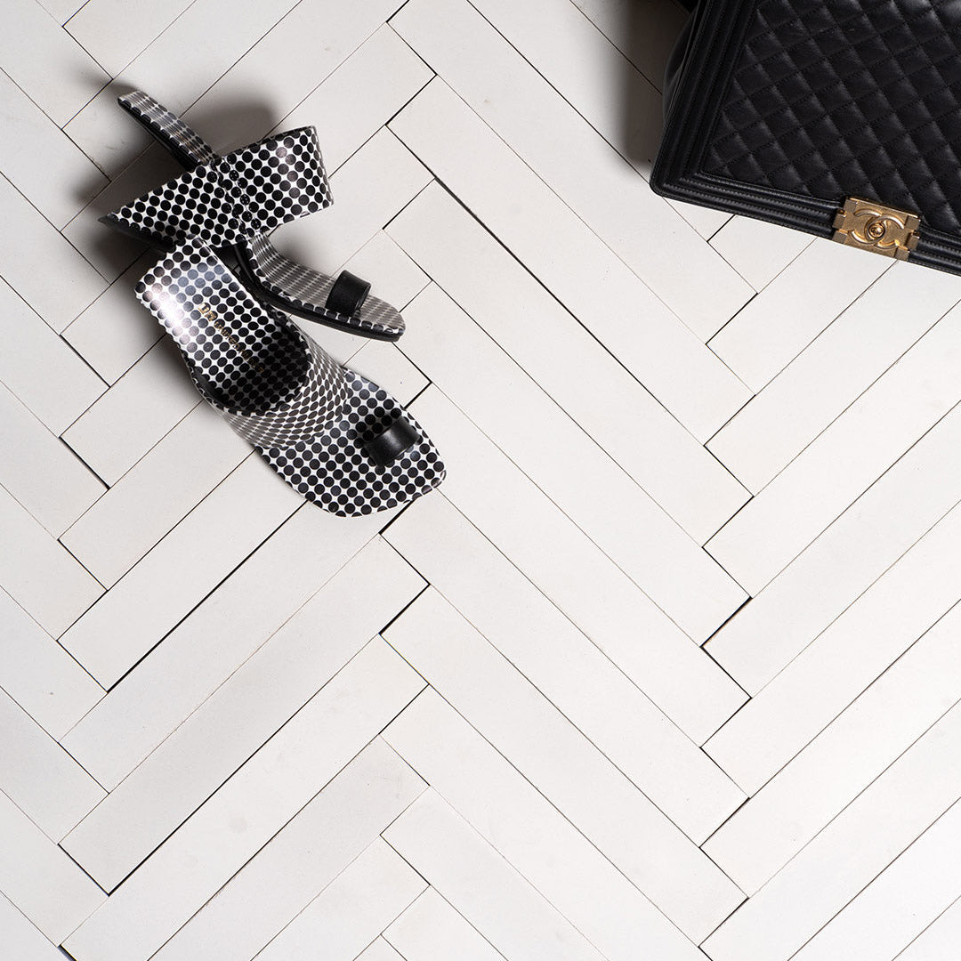 Dirty white cement tiles arranged in a herringbone pattern, showcasing a matte finish and subtle beige undertones, ideal for rustic, modern, or industrial-style flooring and walls.