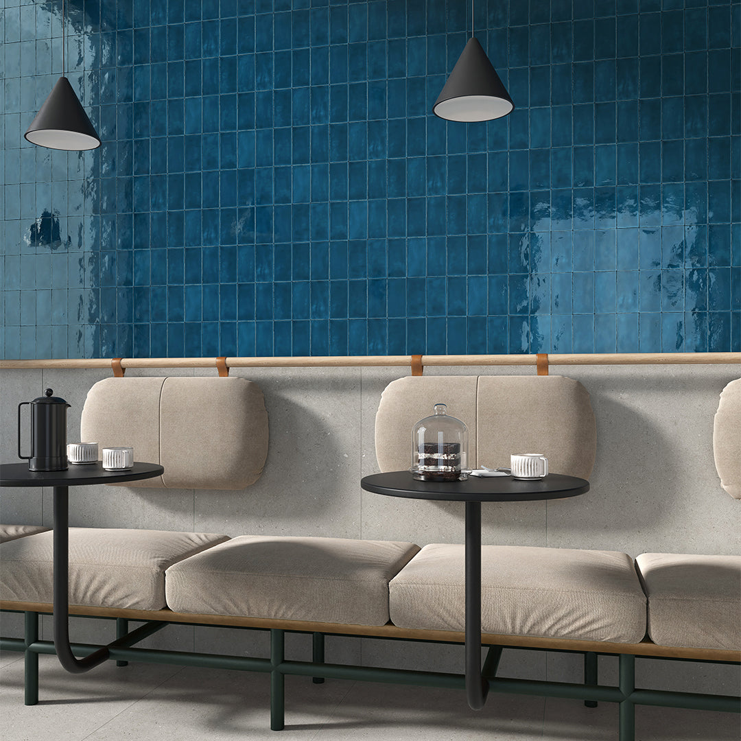 Modern cafe interior with beige sofa, small black tables, and blue tiled wall.