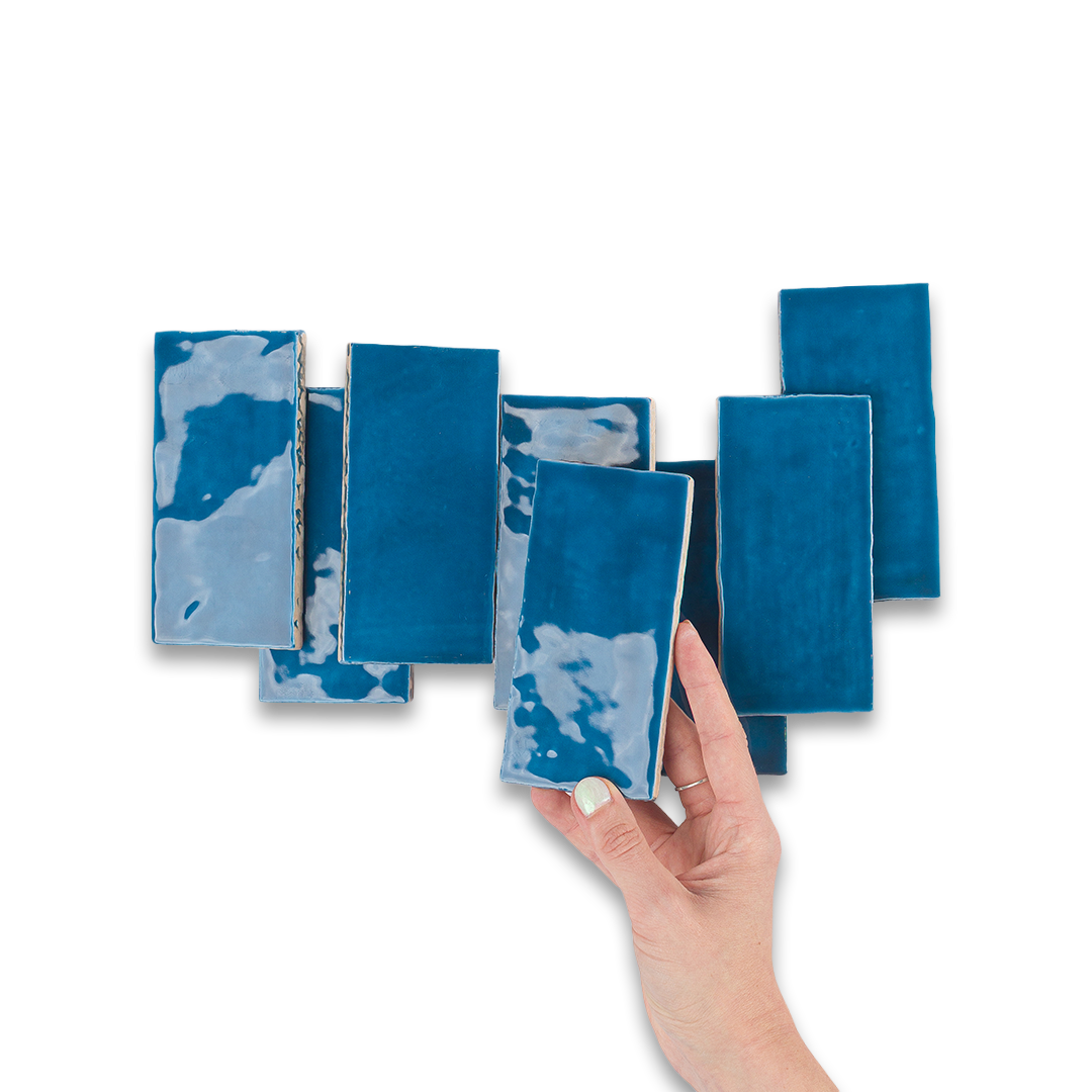 Hand holding a blue ceramic tile with more tiles displayed on a white background