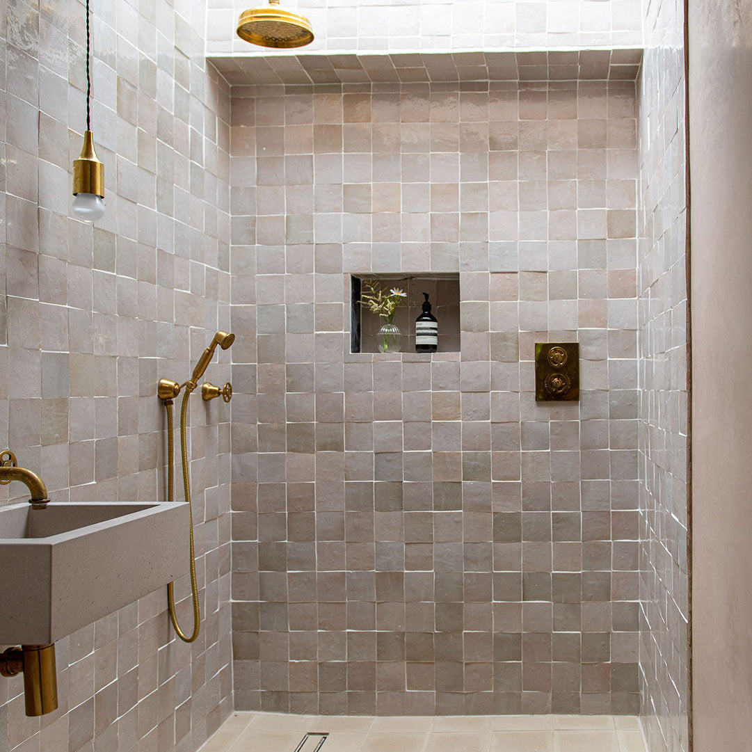 Modern shower with tiled walls, gold fixtures, and a sink.
