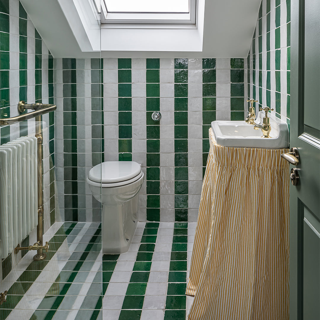 Bathroom with green and white tiles, a toilet, sink, and striped shower curtain.
