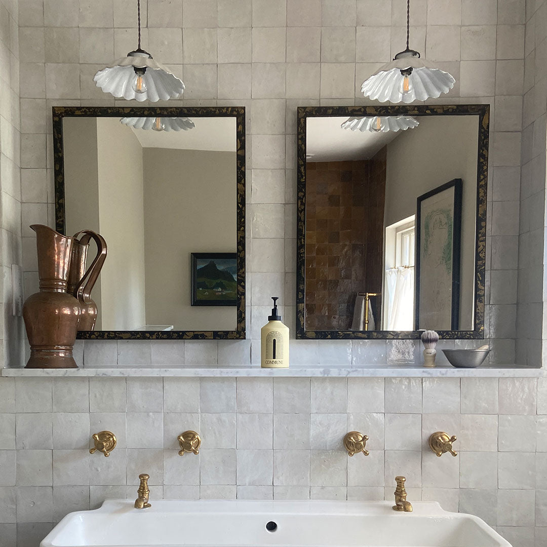Bathroom with white sink, gold fixtures, and two mirrors on a tiled wall.