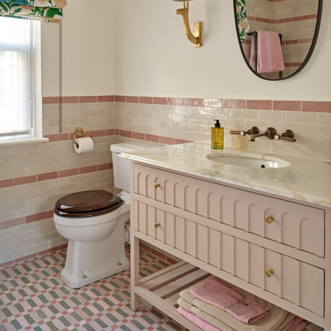 Bathroom with pink tiled walls, wooden vanity, and toilet.