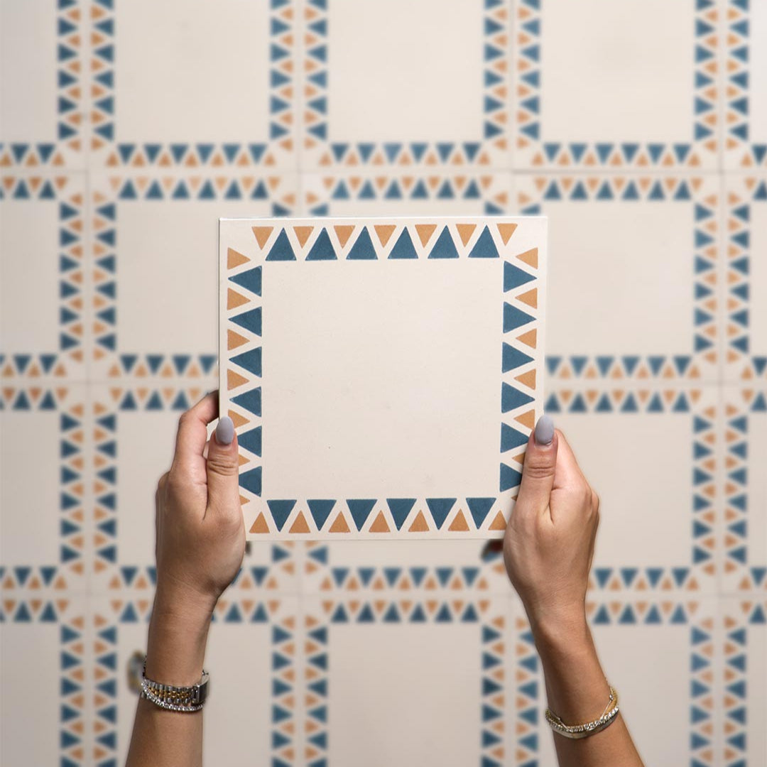 Square cement tile featuring a cream base with a geometric border of alternating blue and terracotta triangles, handcrafted matte finish, ideal for Mediterranean, bohemian, or contemporary interior flooring and wall décor.