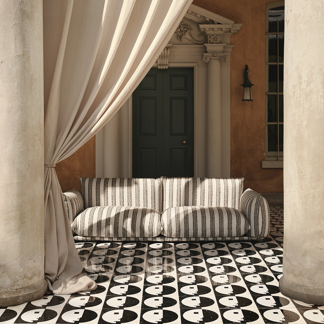 Striped sofa in a classical setting with draped curtains and a patterned floor.