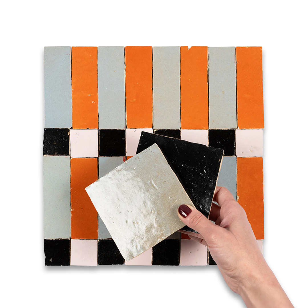 Hand holding a sample of tile against a patterned tile background