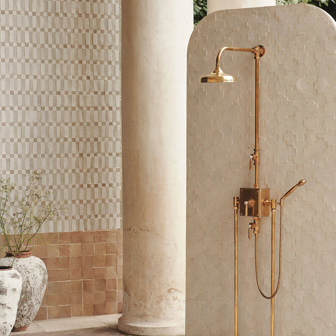 Gold shower system mounted on a tiled wall with decorative elements.