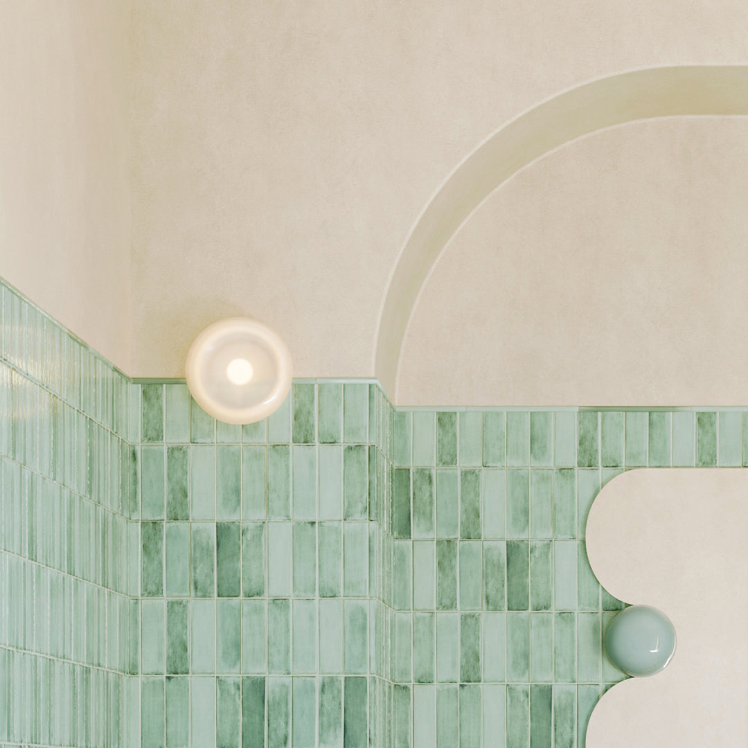 Green tiled wall with a circular light fixture and abstract sculpture.