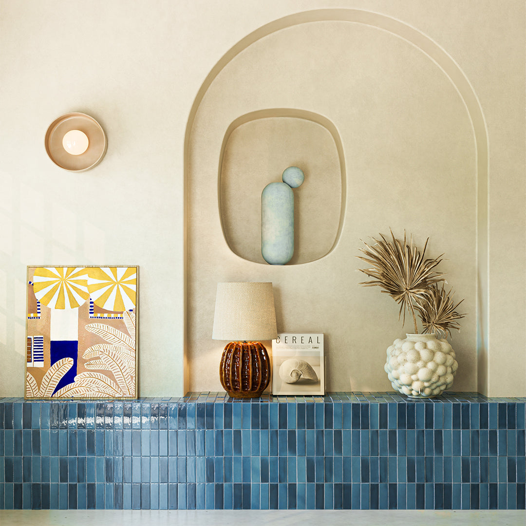 Decorative wall with blue tiled shelf, framed artwork, and decorative items.