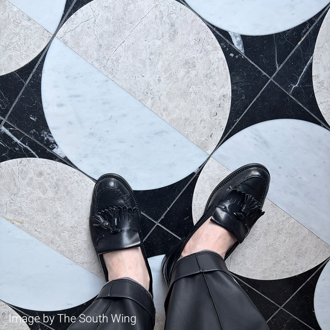 Black loafers on a person standing on a geometric-patterned floor.
