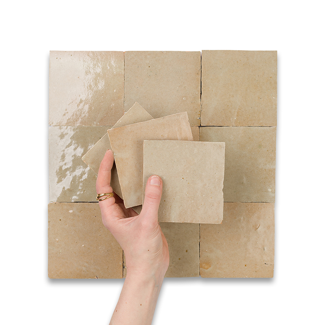 Hand holding brown paper against a tiled wall with a white background