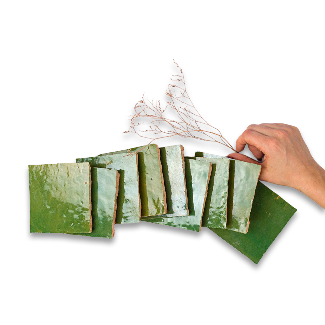 Hand holding a dried plant over a set of green ceramic tiles on a white background