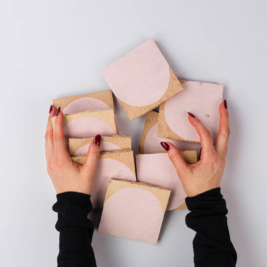 Hands holding pink and beige jewelry display cards on a light gray background