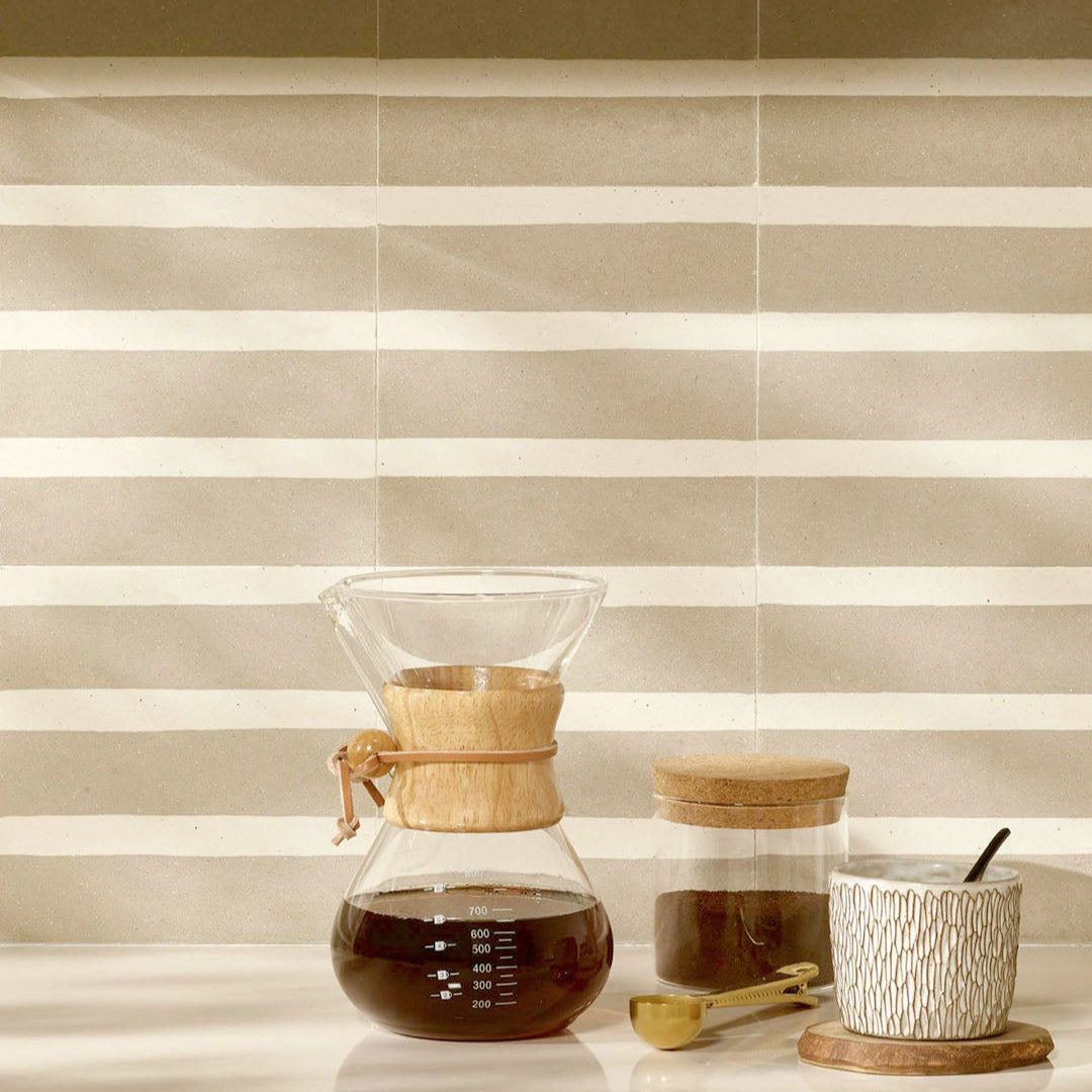 Coffee-making setup with a glass carafe, wooden scoop, and small container on a striped surface.