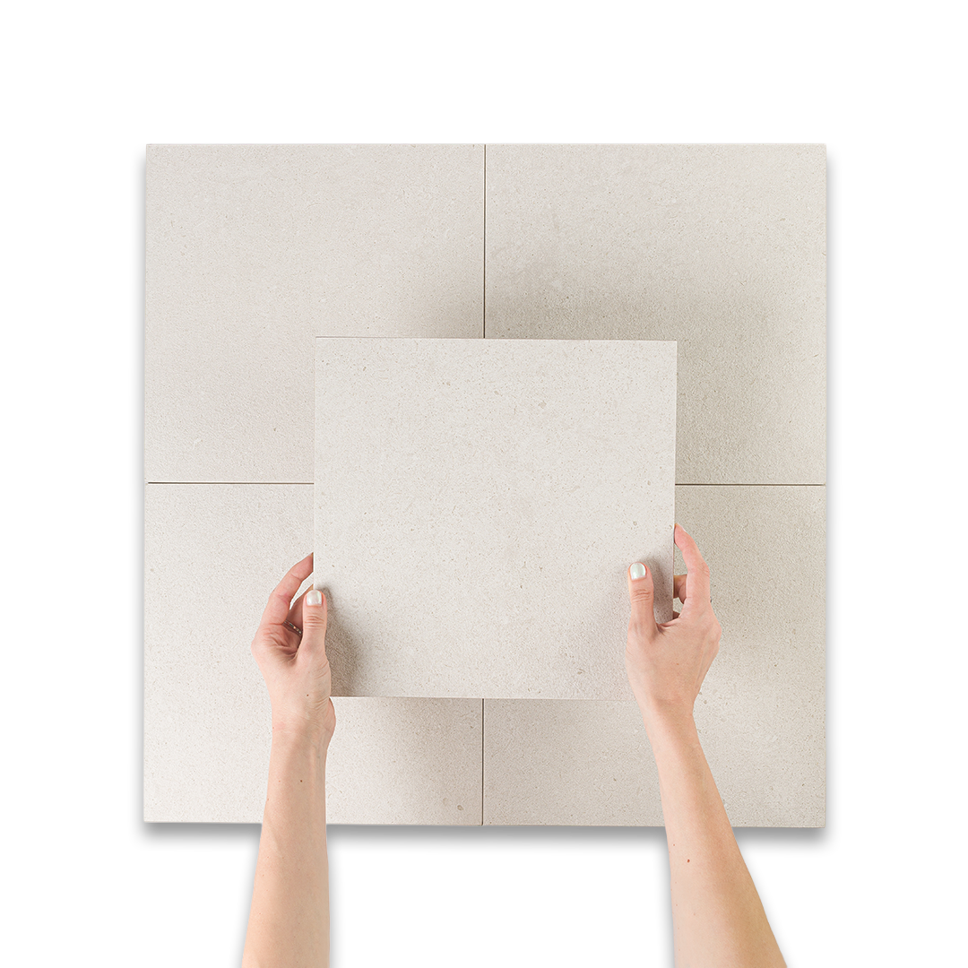 Hands holding a square tile against a larger tiled wall.