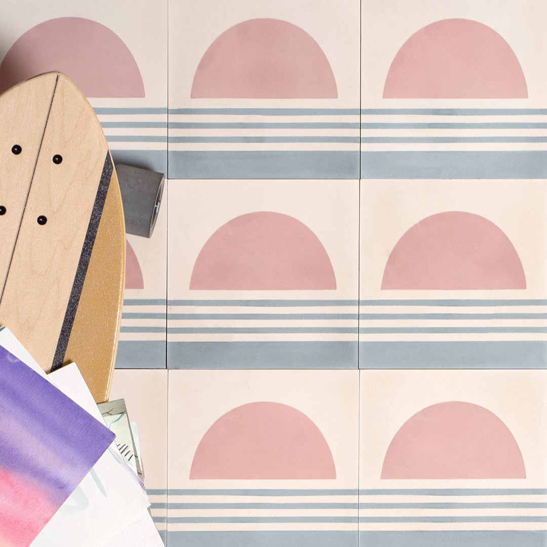 Sunset Stripes cement tile featuring a large pink semicircle sun above soft blue horizontal lines on a cream base, matte finish, ideal for coastal, bohemian, or modern interior wall and floor décor.
