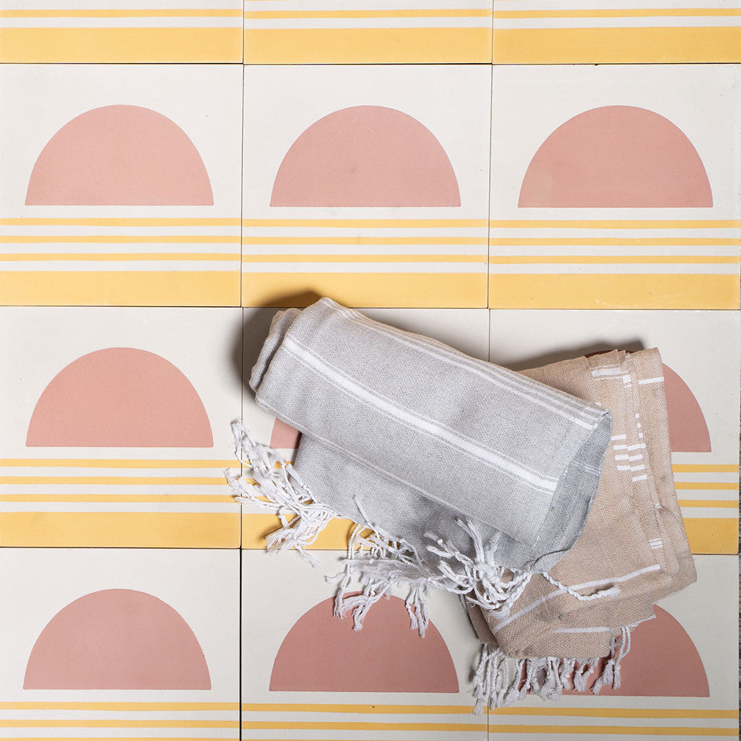 Square cement tile featuring a minimalist sunset design with a pink semicircle sun above soft yellow horizontal stripes, matte finish, ideal for modern, coastal, or bohemian interior wall and floor décor.