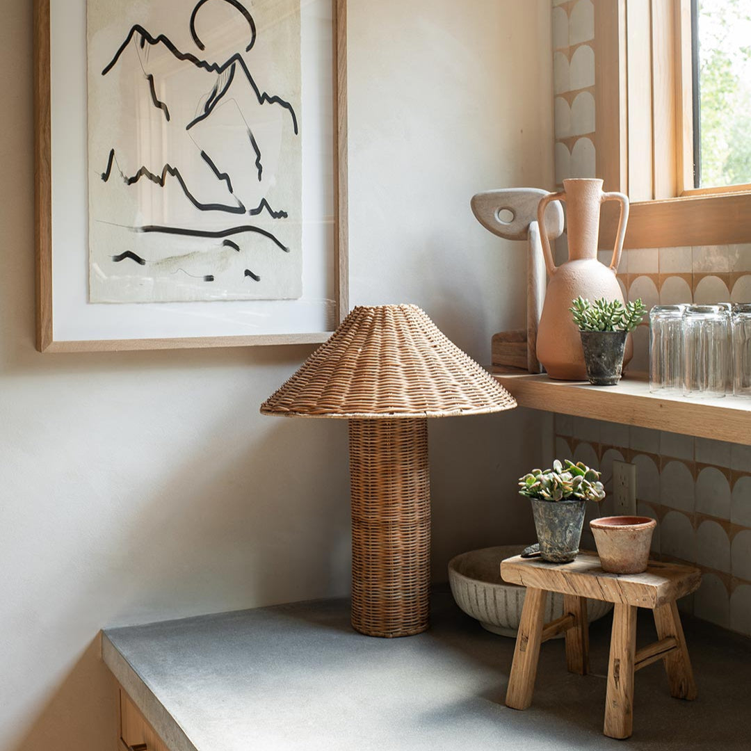 Rattan lamp next to a wooden stool with plants in a room setting.