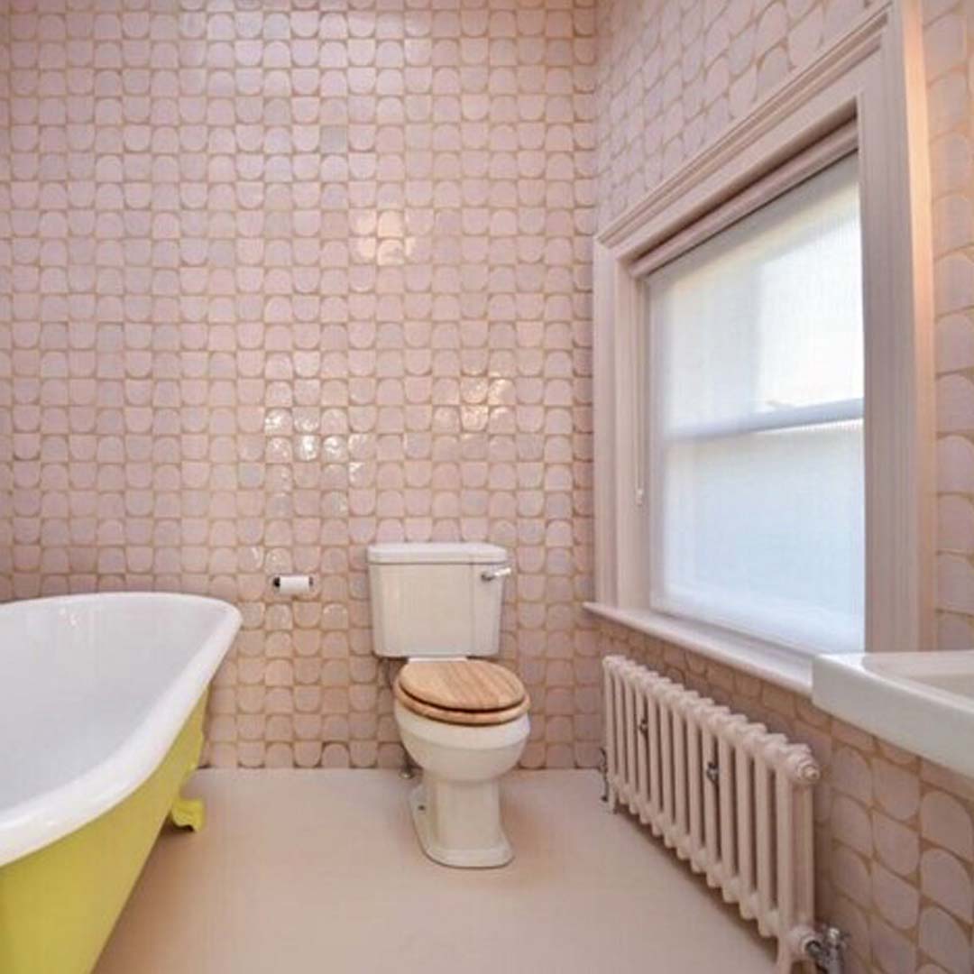 Bathroom with pink tiled walls, a yellow bathtub, and a white toilet.