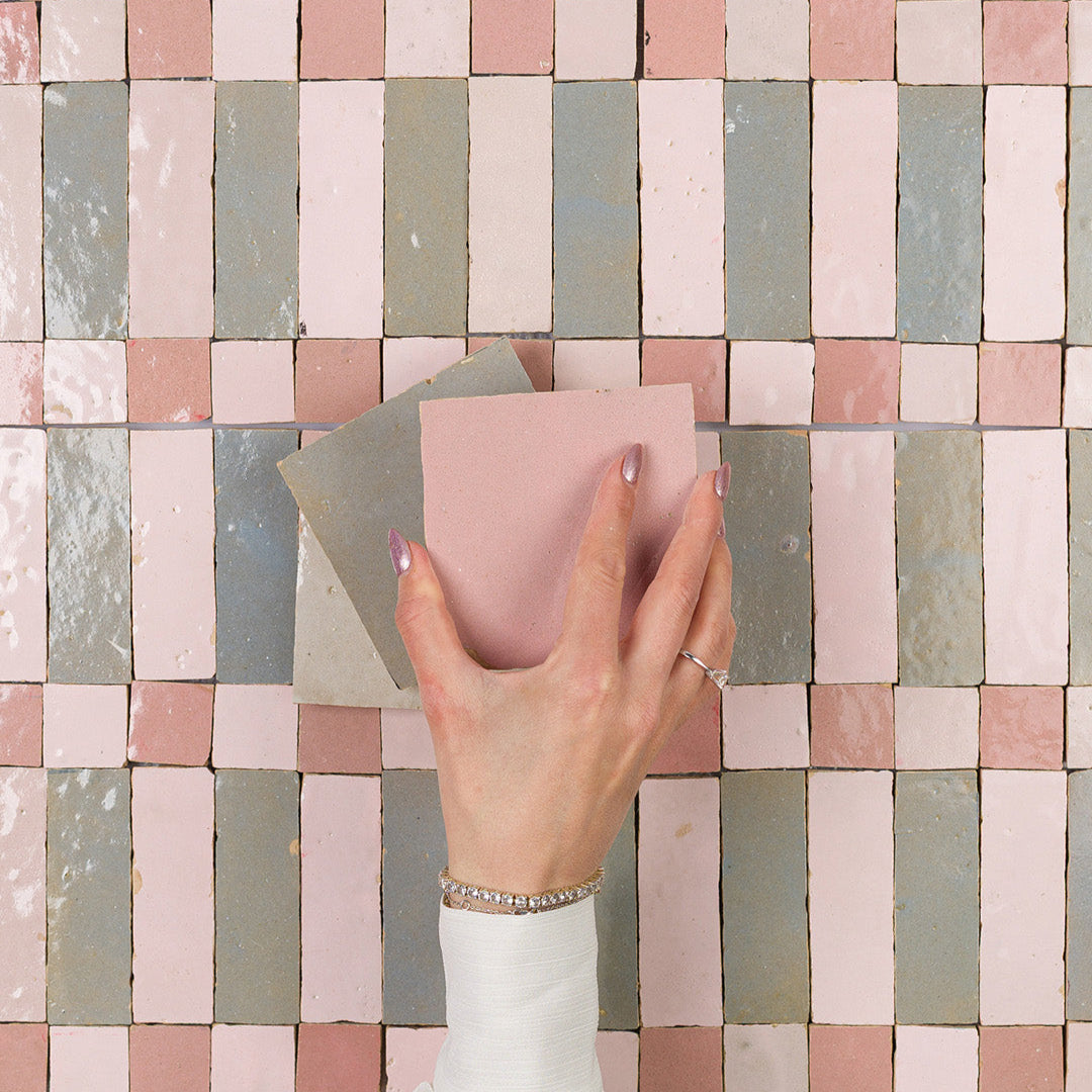 Hand holding a pink tile against a patterned tile wall