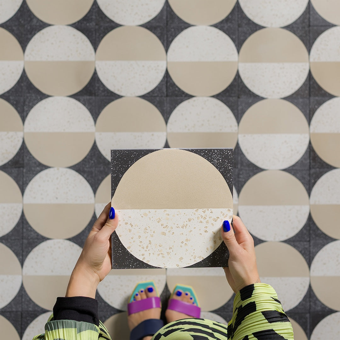 Square tile with a circular design split between dark gray and beige terrazzo patterns. 