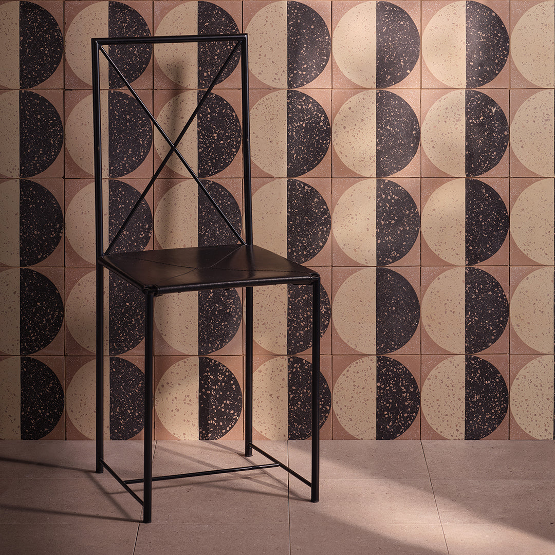 A square cement tile featuring a large circle divided into black and beige halves with terrazzo speckles, set against a warm brown background for a modern geometric look.