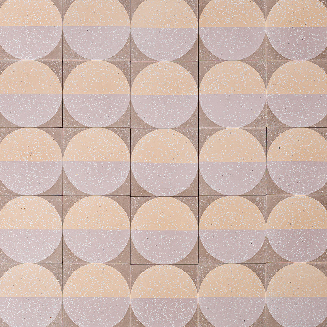 A square cement tile featuring a large circle divided into peach and mauve halves with white terrazzo speckles, set against a taupe background for a modern geometric look.
